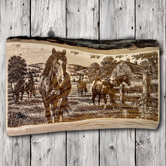 Handcrafted live edge hardwood wall art featuring detailed laser engraving of horses in a country pasture with a rustic barn, wooden fences, and rolling hills.