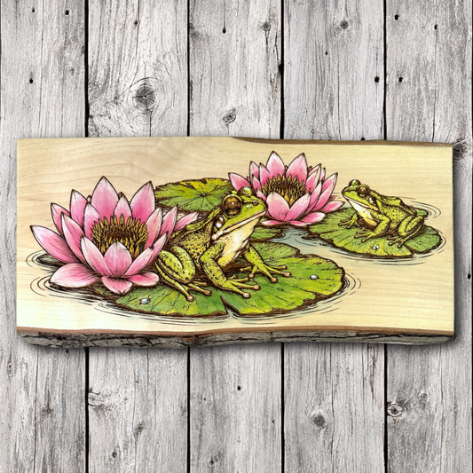 Hand-painted live edge wood wall art featuring two green frogs resting on lily pads among vibrant pink water lilies, with detailed laser engraving on natural hardwood.