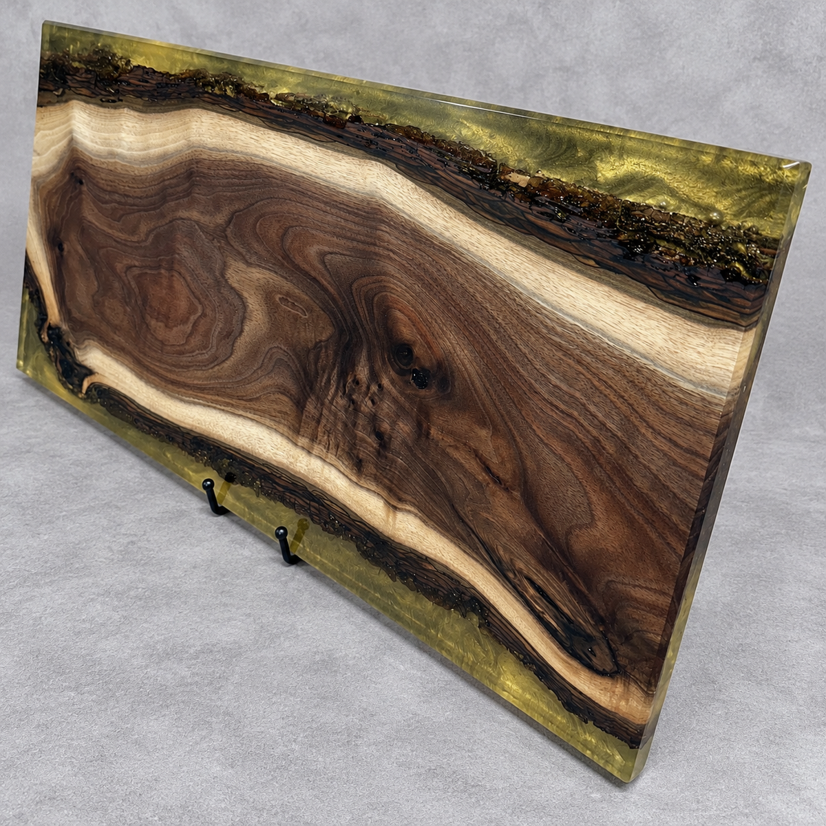 Handcrafted Golden Enchantment wood and epoxy art serving board featuring richly figured chocolate-brown wood with creamy natural edges, surrounded by shimmering translucent olive-gold epoxy along the upper and lower borders. Handmade by Trees To Home in Pennsylvania.