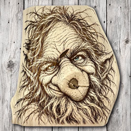Live edge hardwood wall art featuring a detailed laser engraved woodland troll with a large crooked nose, pointed ears, wild hair, expressive blue eyes, and a mischievous smile.